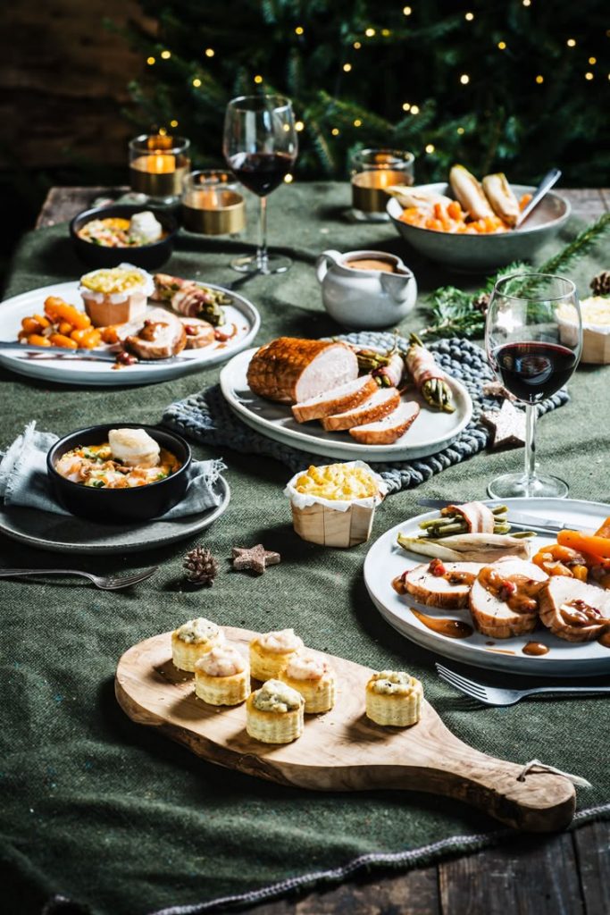 Rustic holiday dinner table spread with sliced roast turkey, gravy, side dishes, wine glasses, and puff pastry appetizers